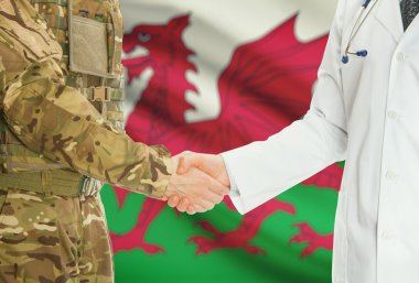 Military man in uniform and doctor shaking hands with national flag on background - Wales