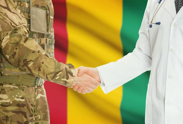 Military man in uniform and doctor shaking hands with national flag on background - Guinea — Stock Photo, Image
