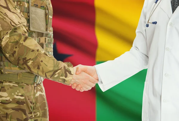 Military man in uniform and doctor shaking hands with national flag on background - Guinea-Bissau — 图库照片