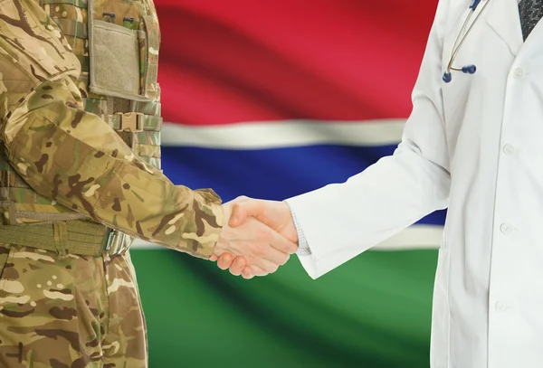 Military man in uniform and doctor shaking hands with national flag on background - Gambia — Stock Photo, Image