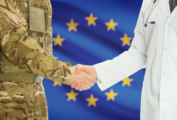Military man in uniform and doctor shaking hands with national flag on background - European Union - EU — ストック写真