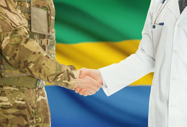 Military man in uniform and doctor shaking hands with national flag on background - Gabon — Stok fotoğraf