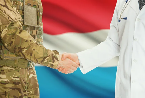 Military man in uniform and doctor shaking hands with national flag on background - Luxembourg — Stok fotoğraf