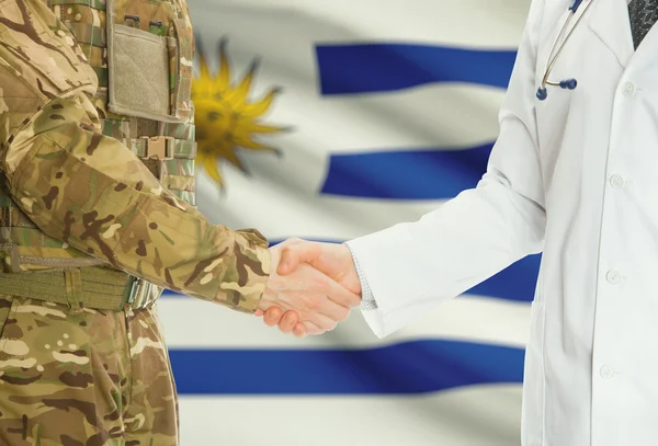 Military man in uniform and doctor shaking hands with national flag on background - Uruguay
