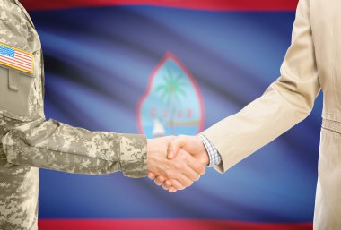 USA military man in uniform and civil man in suit shaking hands with national flag on background - Guam