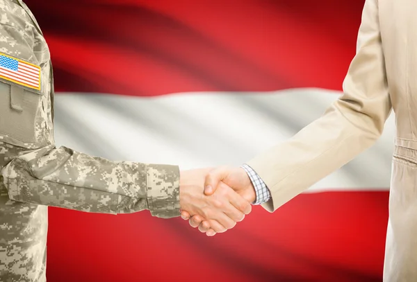 USA military man in uniform and civil man in suit shaking hands with national flag on background - Austria — Stockfoto