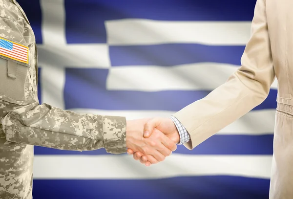 USA military man in uniform and civil man in suit shaking hands with national flag on background - Greece —  Fotos de Stock