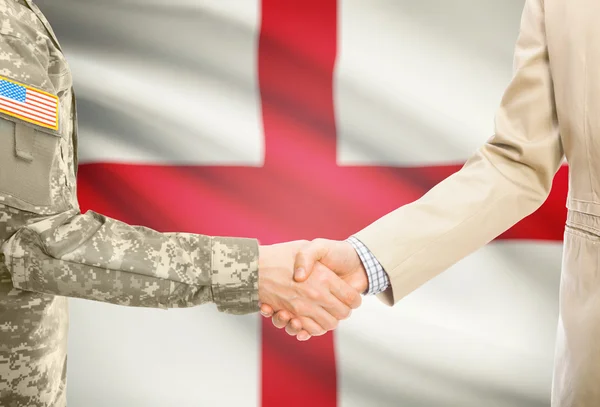 USA military man in uniform and civil man in suit shaking hands with national flag on background - England —  Fotos de Stock