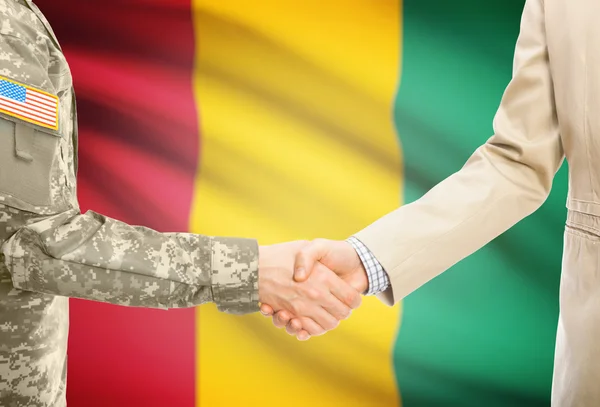 США военный человек в военной форме и гражданской мужчина в костюме, рукопожатие с национальным флагом на фоне - Гвинея — стоковое фото