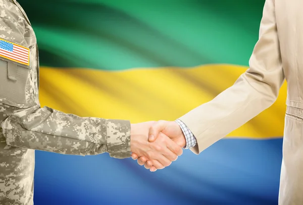 USA military man in uniform and civil man in suit shaking hands with national flag on background - Gabon — Stock fotografie