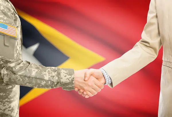 USA military man in uniform and civil man in suit shaking hands with national flag on background - East Timor —  Fotos de Stock