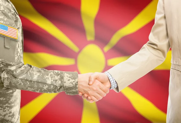 USA military man in uniform and civil man in suit shaking hands with national flag on background - Macedonia — Foto Stock