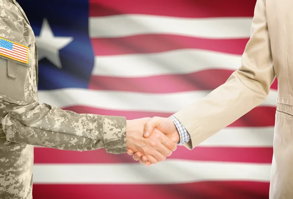 США военный человек в военной форме и гражданской мужчина в костюме, рукопожатие с национальным флагом на фоне - Либерия — стоковое фото