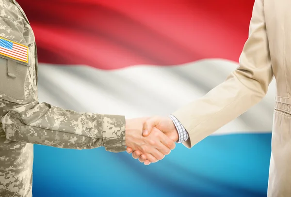 США военный человек в военной форме и гражданской мужчина в костюме, рукопожатие с национальным флагом на фоне - Люксембург — стоковое фото