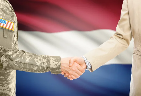 USA military man in uniform and civil man in suit shaking hands with national flag on background - Netherlands — Stock fotografie