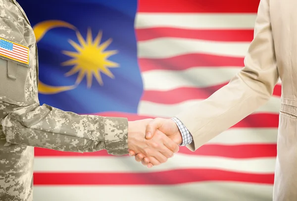 USA military man in uniform and civil man in suit shaking hands with national flag on background - Malaysia — Stock Photo, Image