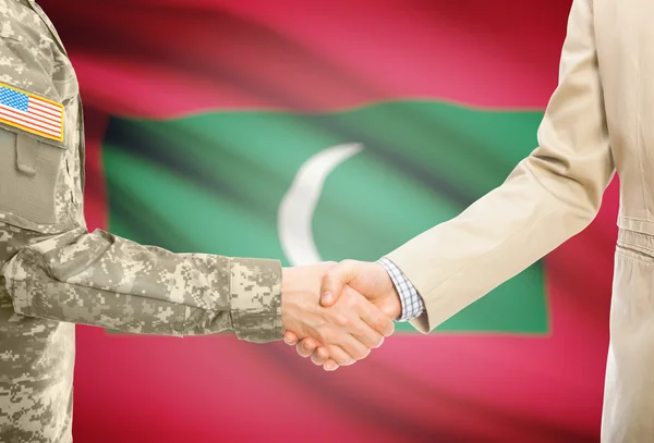 USA military man in uniform and civil man in suit shaking hands with national flag on background - Maldives — Stock Photo, Image
