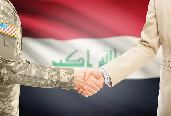 USA military man in uniform and civil man in suit shaking hands with national flag on background - Iraq — Stockfoto