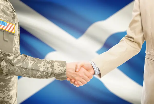 USA military man in uniform and civil man in suit shaking hands with national flag on background - Scotland — Stockfoto