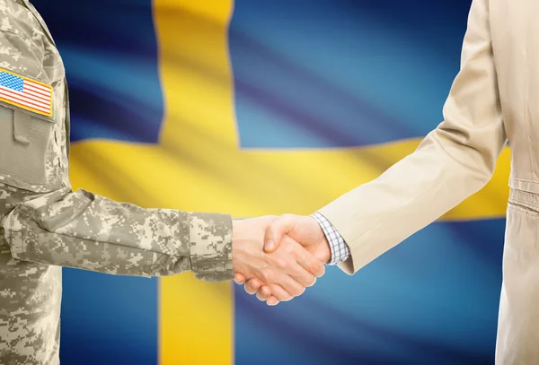 USA military man in uniform and civil man in suit shaking hands with national flag on background - Sweden — Stock fotografie