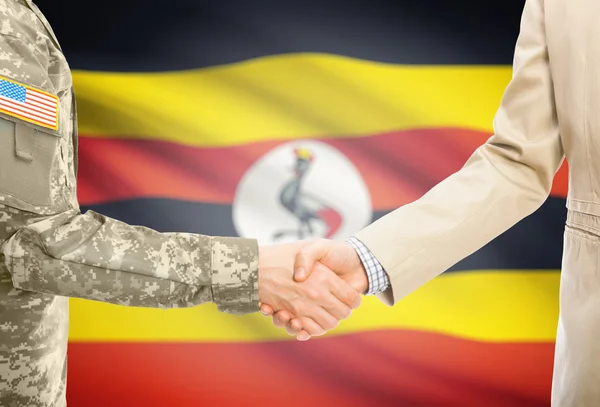 USA military man in uniform and civil man in suit shaking hands with national flag on background - Uganda — ストック写真