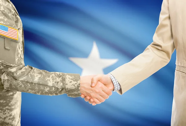 USA military man in uniform and civil man in suit shaking hands with national flag on background - Somalia — Stock Photo, Image