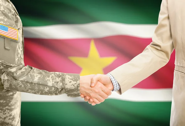 Hombre militar de usa en uniforme y civil hombre en traje sacudiendo las manos con bandera nacional de fondo - Surinam —  Fotos de Stock