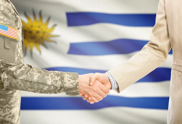 USA military man in uniform and civil man in suit shaking hands with national flag on background - Uruguay — Stock Photo, Image