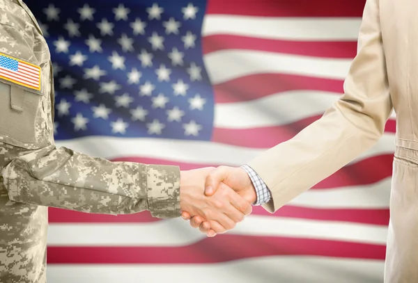 USA military man in uniform and civil man in suit shaking hands with national flag on background - United States - Stock-foto