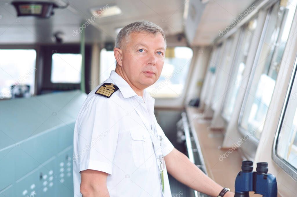 The captain of a cargo ship in a white shirt keeps order from the captain's bridge.