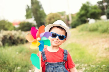 Kot pantolon, güneş gözlüğü ve rüzgar çiçekli oyuncağı olan bir yaz parkında beyaz şapkalı şirin, mutlu erkek bebek..