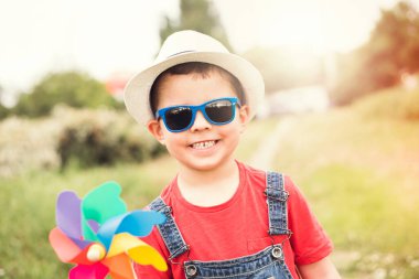 Kot pantolon, güneş gözlüğü ve rüzgar çiçekli oyuncağı olan bir yaz parkında beyaz şapkalı şirin, mutlu erkek bebek..