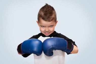 Kafasında mavi boks eldiveni ve siyah-beyaz tişörtü olan, çok kötü görünüşlü, küçük, sportif bir çocuk..