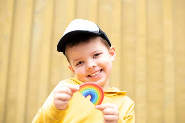 可愛い男の子が笑顔で黄色い背景に手にプラスチック製の虹を持っています — ストック写真