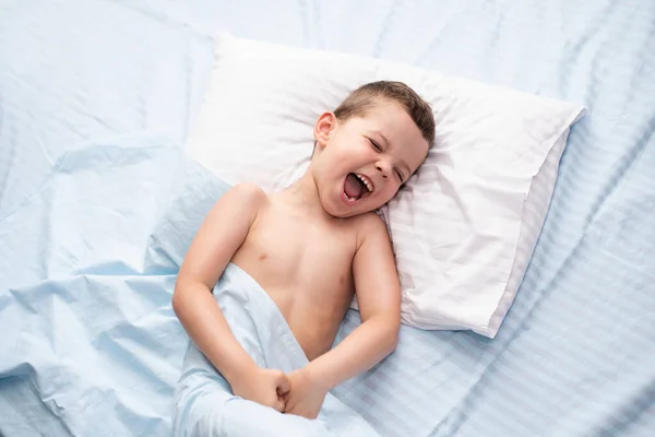 美しい青いベッドの上に寝そべっていると ５歳の少年が悲鳴を上げる 子供は寝たくない — ストック写真