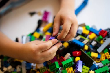 Bir sürü renkli yapı bloğunun arka planına karşı lego yapan bir çocuğun elleri.