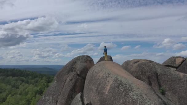 Yalnız bir adam dağın tepesinde duruyor ve ormanın güzel manzarasının tadını çıkarıyor.. — Stok video