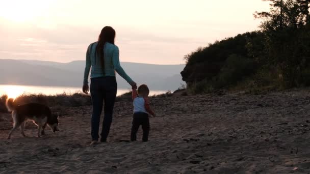 İki oğlu olan genç bir kadın gün batımında sahilde yürüyor.. — Stok video