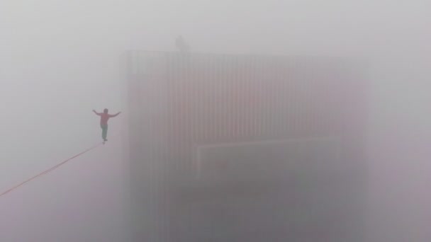 Tiro de dron de un atleta extremo masculino atrapa su equilibrio en un cabestrillo estirado a un rascacielos a una gran altitud. — Vídeos de Stock