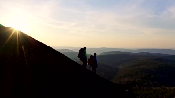 배낭을 든 두 젊은 등산객 이 석양에 바위 언덕을 내려오고 있다. — 비디오