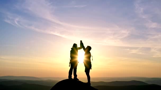 Silhouetten van een jong echtpaar die elkaar de hand schudden en bij zonsondergang op een bergtop omhelzen. — Stockvideo