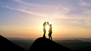 Gün batımında bir adam ve kadının yavaş çekimleri zaferle el sıkışıyor ve bir dağın tepesinde duruyor..