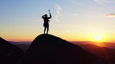 Dişi bir dağcının, buz baltasını tutarak ellerini havaya kaldırmasını gösteren robot resmi..