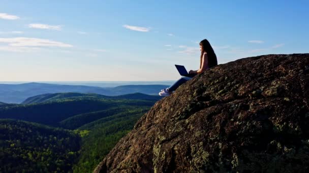 어느 젊고 매력적 인 프리랜서 여자 가산 꼭대기에 앉아 있는 동안 노트북을 펴서 손을 뻗고 있는 모습을 공중에서 본 모습 — 비디오