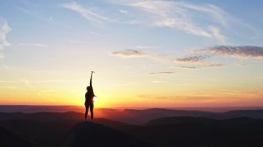 Yavaş çekim dağcı kadın silueti neşe içinde bir buz baltasını kaldırır ve gün batımında zaferi kutlar.
