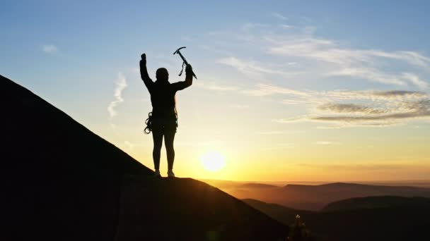 一位女登山者站在山坡上慢慢地举起冰斧. — 图库视频影像