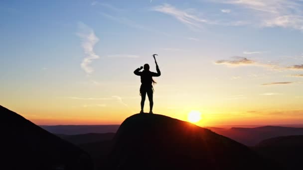 Silhouet van een vrouwelijke klimmer die de overwinning viert op de top van de berg bij zonsondergang — Stockvideo