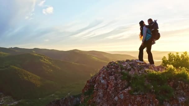 Drone shot van een jonge moeder met haar jonge zoon in een carrier wandelen op een bergpad bij zonsondergang — Stockvideo