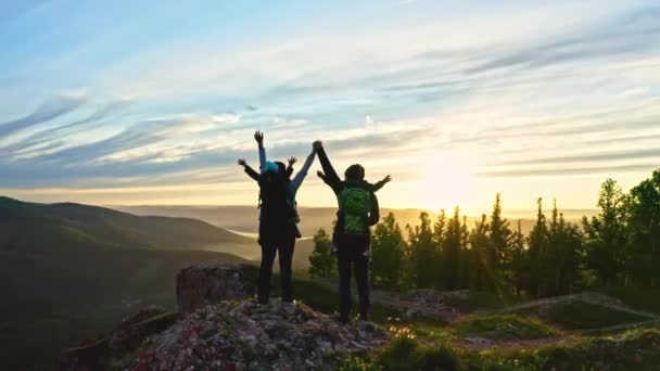 Een jong stel met twee zoons steekt graag hun handen op als ze bij zonsondergang op de top van de berg staan — Stockvideo