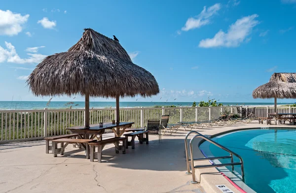 Mesa de playa con sombrilla de heno junto a una piscina — Foto de Stock
